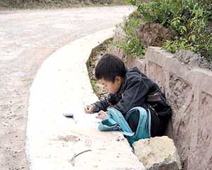 山里男孩趴在路沿上写作业称外面比家里亮(图)
